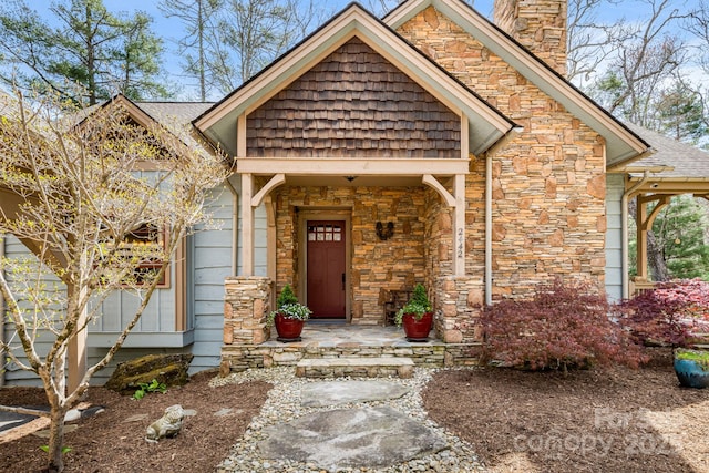 property entrance with roof with shingles, a chimney, and stone siding