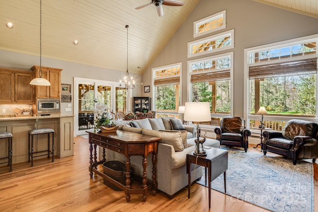 living area with high vaulted ceiling, plenty of natural light, light wood-style flooring, and ceiling fan with notable chandelier