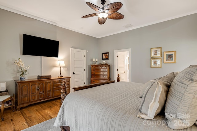 bedroom featuring crown molding, ensuite bath, a ceiling fan, wood finished floors, and visible vents