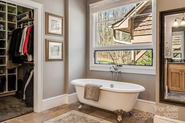 bathroom featuring a walk in closet, stone finish floor, vanity, baseboards, and a soaking tub