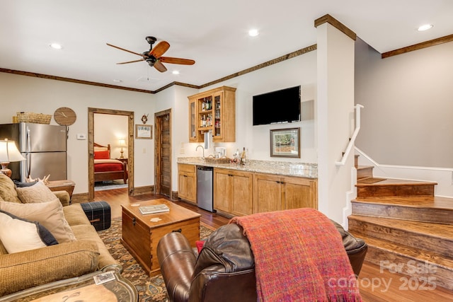 living room featuring a ceiling fan, dark wood-style flooring, crown molding, stairway, and indoor wet bar