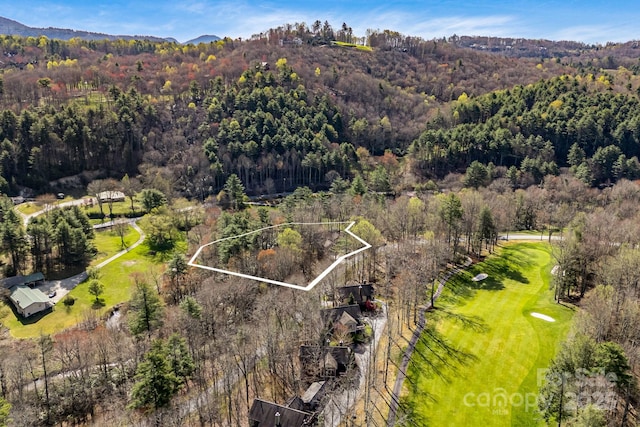 drone / aerial view with a mountain view, golf course view, and a wooded view