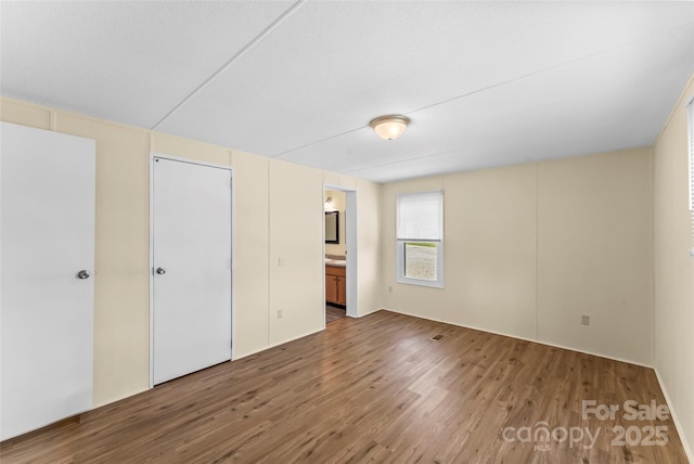 unfurnished bedroom with connected bathroom and wood finished floors
