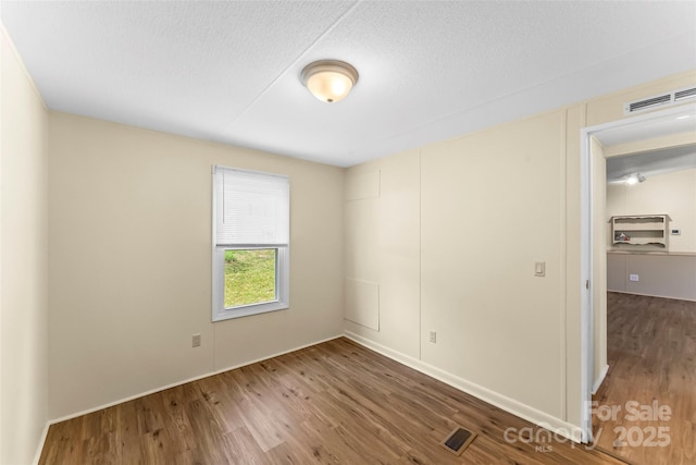 spare room with visible vents, a textured ceiling, and wood finished floors