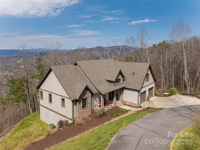 modern farmhouse with stone siding, a garage, concrete driveway, a shingled roof, and a mountain view