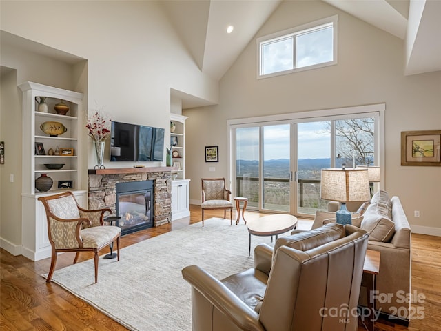 living area with high vaulted ceiling, baseboards, built in features, a fireplace, and wood finished floors