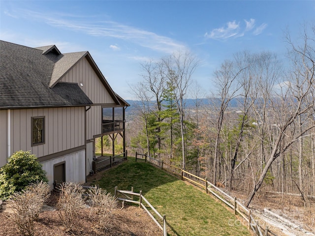 view of side of home with a yard, fence, board and batten siding, and roof with shingles