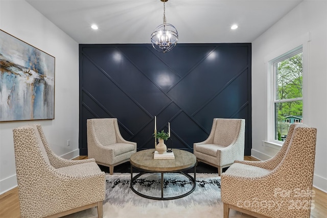 sitting room featuring light wood-style flooring, baseboards, recessed lighting, an accent wall, and a notable chandelier