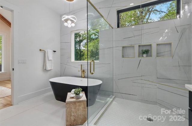 full bath featuring baseboards, a freestanding bath, a walk in shower, and an inviting chandelier