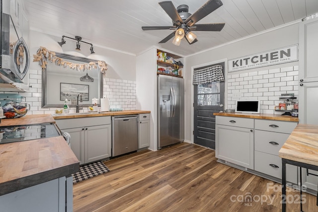kitchen featuring wood counters, decorative backsplash, crown molding, a ceiling fan, and appliances with stainless steel finishes