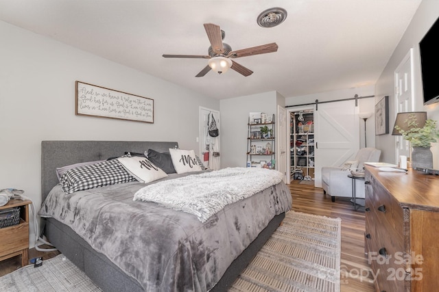 bedroom featuring a barn door, a closet, wood finished floors, a spacious closet, and a ceiling fan
