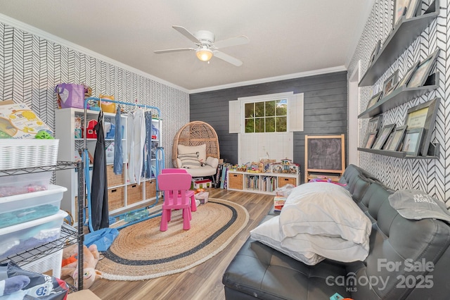 playroom with wood finished floors, ceiling fan, crown molding, and wallpapered walls