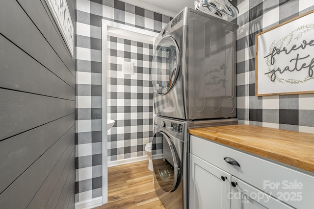 clothes washing area with stacked washing maching and dryer, light wood-style flooring, cabinet space, and wallpapered walls