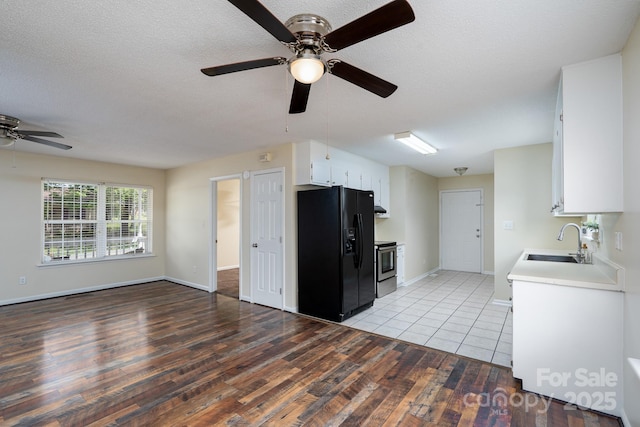 kitchen with black refrigerator with ice dispenser, a sink, ceiling fan, light wood-style floors, and electric stove