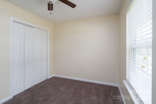 unfurnished bedroom with dark colored carpet, a closet, a ceiling fan, and baseboards