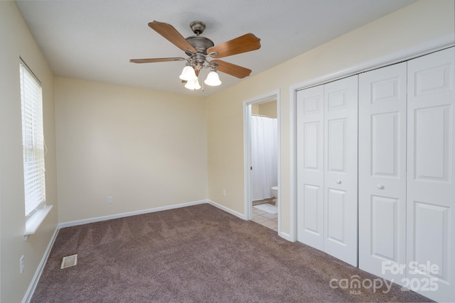 unfurnished bedroom with carpet, a closet, baseboards, ensuite bath, and a ceiling fan