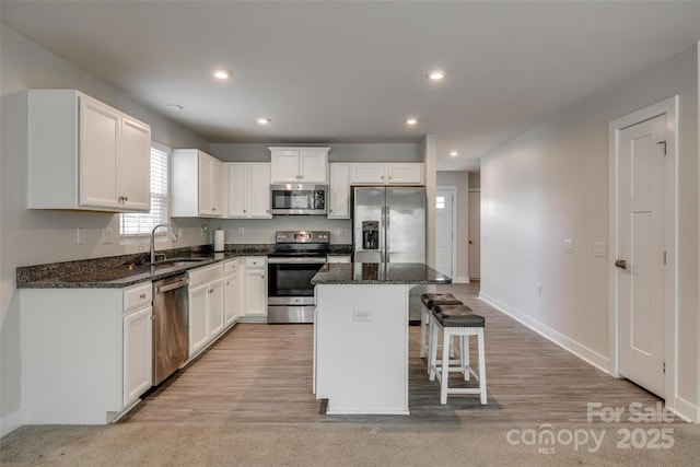 kitchen featuring a center island, a sink, white cabinetry, a breakfast bar, and appliances with stainless steel finishes