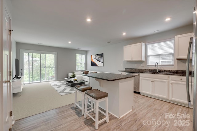 kitchen with stainless steel dishwasher, a sink, a kitchen island, dark stone counters, and white cabinetry