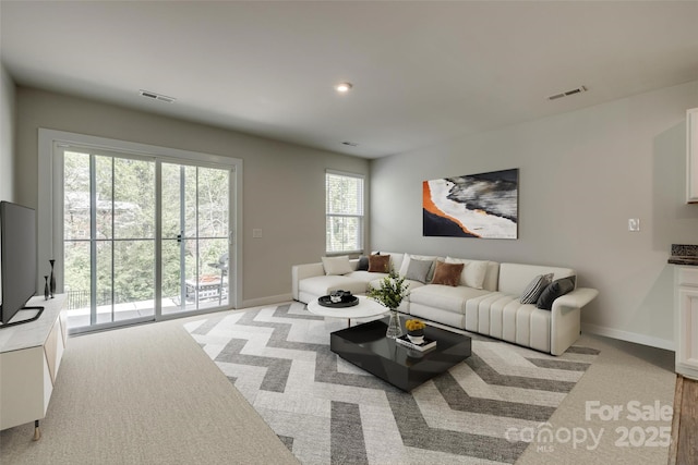 living area with baseboards, visible vents, and light colored carpet