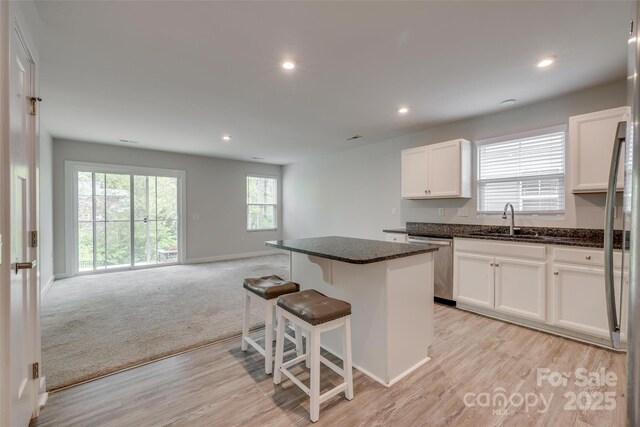 kitchen with stainless steel dishwasher, a sink, open floor plan, white cabinetry, and a kitchen island
