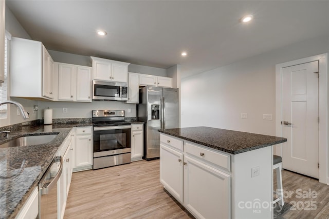 kitchen featuring light wood finished floors, white cabinets, a sink, recessed lighting, and appliances with stainless steel finishes