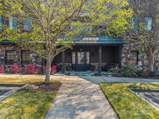 view of front of home with stone siding, metal roof, a standing seam roof, covered porch, and french doors