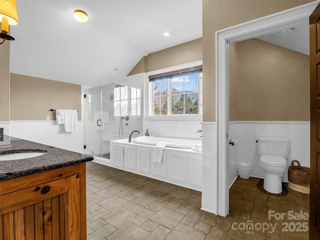 bathroom featuring a bath, a shower stall, toilet, vaulted ceiling, and wainscoting