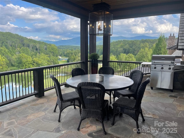 view of patio / terrace featuring grilling area, outdoor dining area, a forest view, and a mountain view