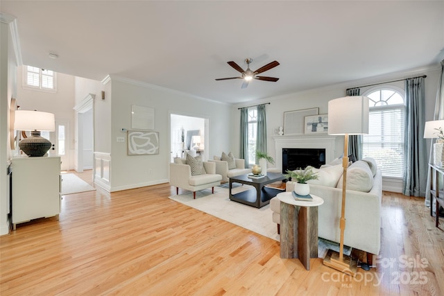 living area featuring crown molding, ceiling fan, a fireplace, and wood finished floors