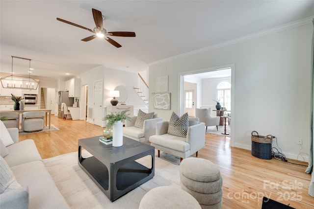 living room featuring crown molding, stairs, baseboards, a ceiling fan, and light wood-style flooring