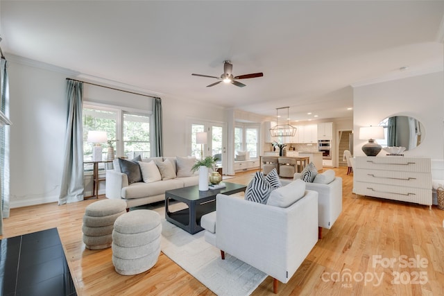 living room featuring light wood-type flooring, ornamental molding, ceiling fan with notable chandelier, and recessed lighting