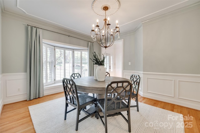 dining room with an inviting chandelier, crown molding, wainscoting, a decorative wall, and light wood-style floors