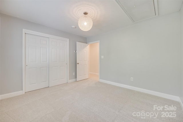 unfurnished bedroom featuring baseboards, light carpet, a closet, and attic access