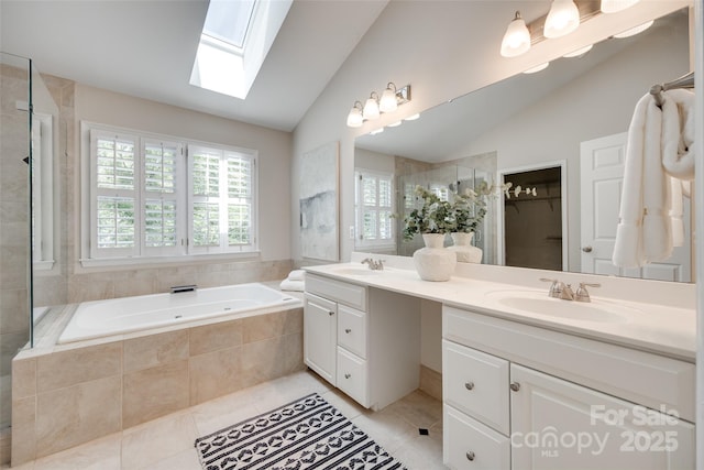 bathroom with tile patterned floors, a sink, vaulted ceiling with skylight, and a garden tub