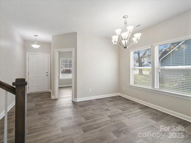unfurnished dining area featuring plenty of natural light, a notable chandelier, baseboards, and wood finished floors