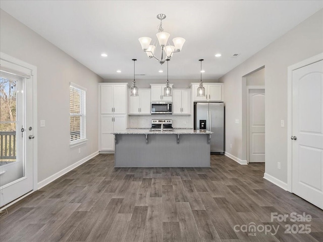 kitchen featuring a kitchen breakfast bar, stainless steel appliances, a center island with sink, white cabinetry, and backsplash