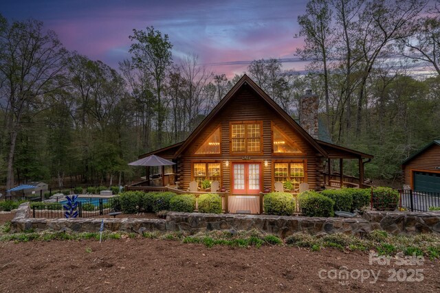 back of house at dusk with a fenced in pool, log siding, a chimney, and french doors