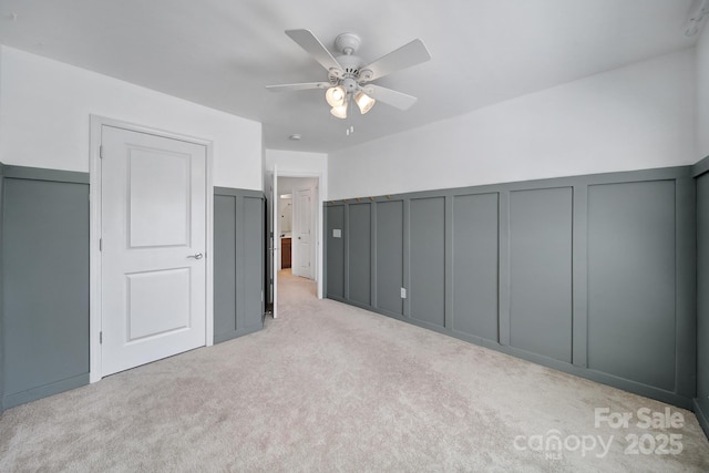interior space featuring a decorative wall, light colored carpet, and a ceiling fan