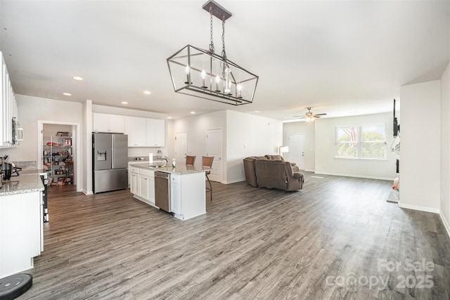 kitchen with white cabinetry, wood finished floors, a sink, stainless steel appliances, and open floor plan
