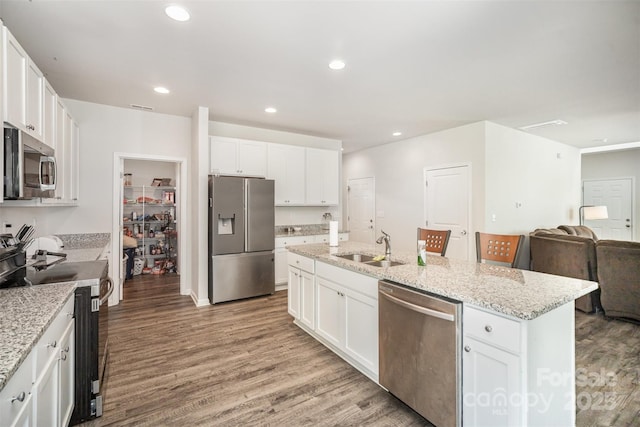 kitchen featuring open floor plan, white cabinetry, stainless steel appliances, light wood finished floors, and a sink