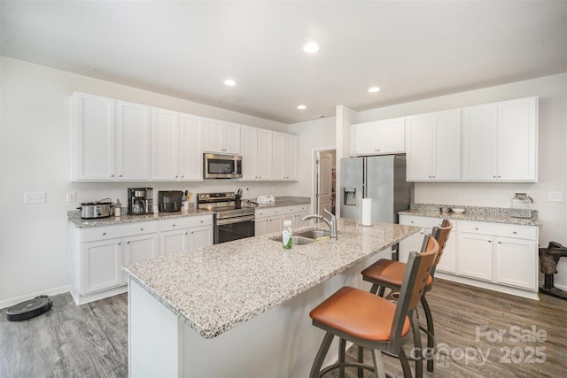 kitchen featuring a breakfast bar, white cabinetry, appliances with stainless steel finishes, a sink, and wood finished floors
