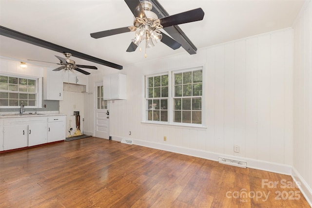 unfurnished living room with wood finished floors, a sink, ceiling fan, plenty of natural light, and beam ceiling