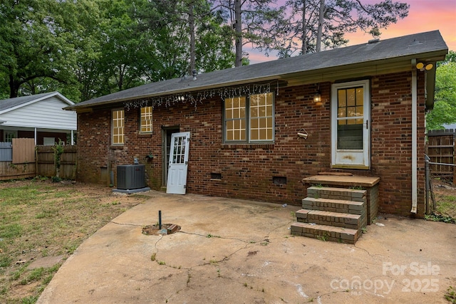 back of property at dusk with fence, brick siding, a patio area, and central AC