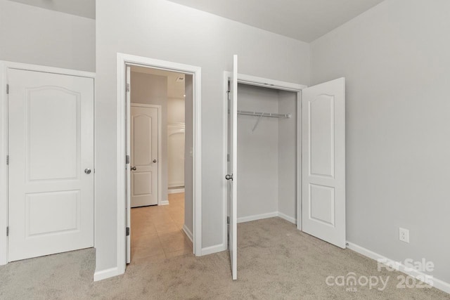 unfurnished bedroom featuring a closet, baseboards, and light colored carpet