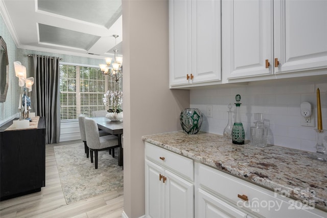 kitchen with white cabinets, a chandelier, crown molding, light stone countertops, and light wood-style flooring