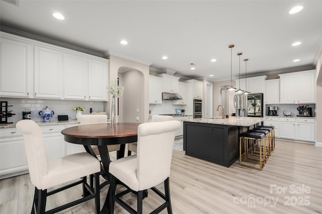 kitchen featuring white cabinets, arched walkways, a sink, an island with sink, and a breakfast bar area
