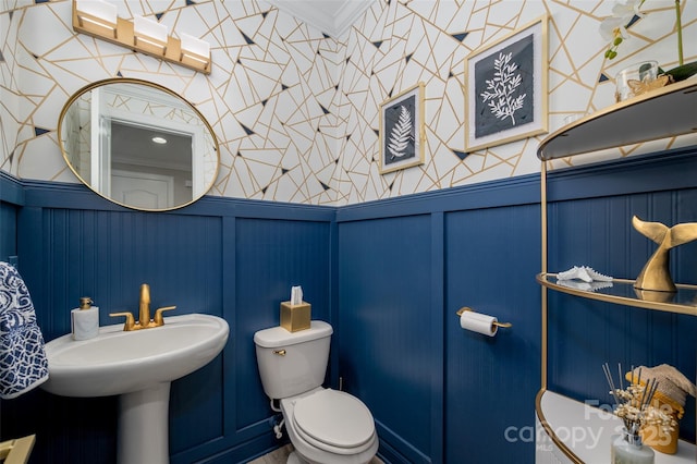 bathroom featuring crown molding, toilet, a decorative wall, and a wainscoted wall
