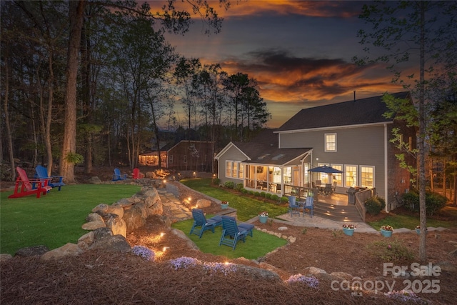 back of house with a fire pit, a wooden deck, and a lawn