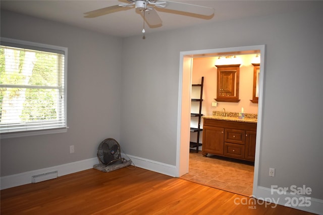 empty room featuring visible vents, baseboards, a sink, light wood-type flooring, and a ceiling fan