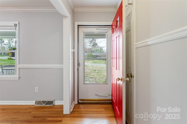 doorway with baseboards, ornamental molding, visible vents, and light wood-style floors